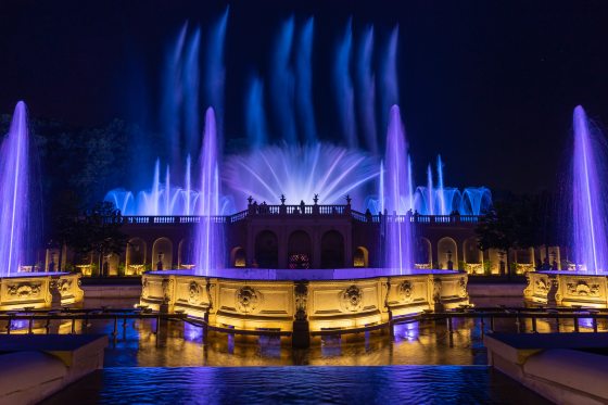 Illuminated fountains in shades of purple shooting up in the air in a variety of designs.