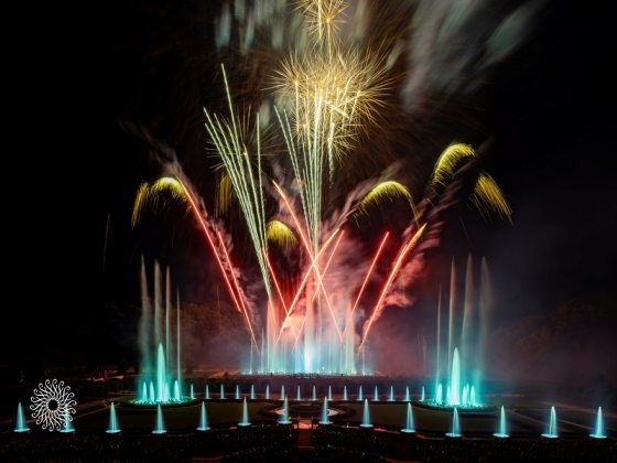 Red, white, and blue fireworks over a series of fountains.