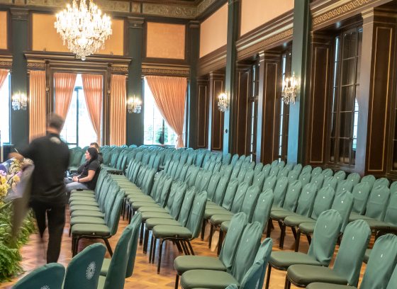 empty green chairs fill an ornate room with wood floors, paneled walls, and a chandelier