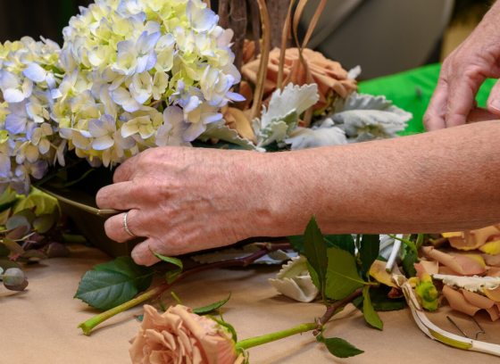 A person creating a floral arrangment out of white and purple hydrangeas.