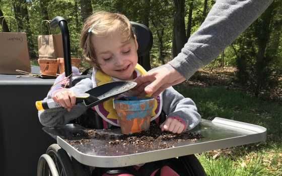 child in wheelchair uses shovel to place soil in hand-painted flowerpot