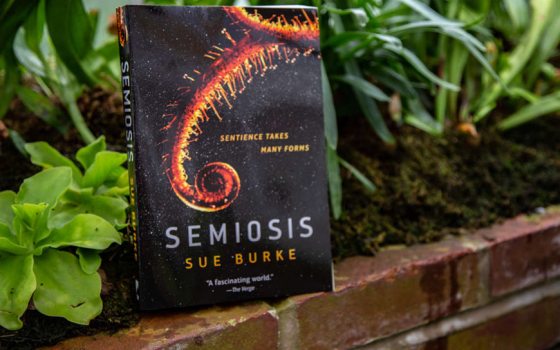 cover of book, "Semiosis" by Sue Burke perched in front of plants