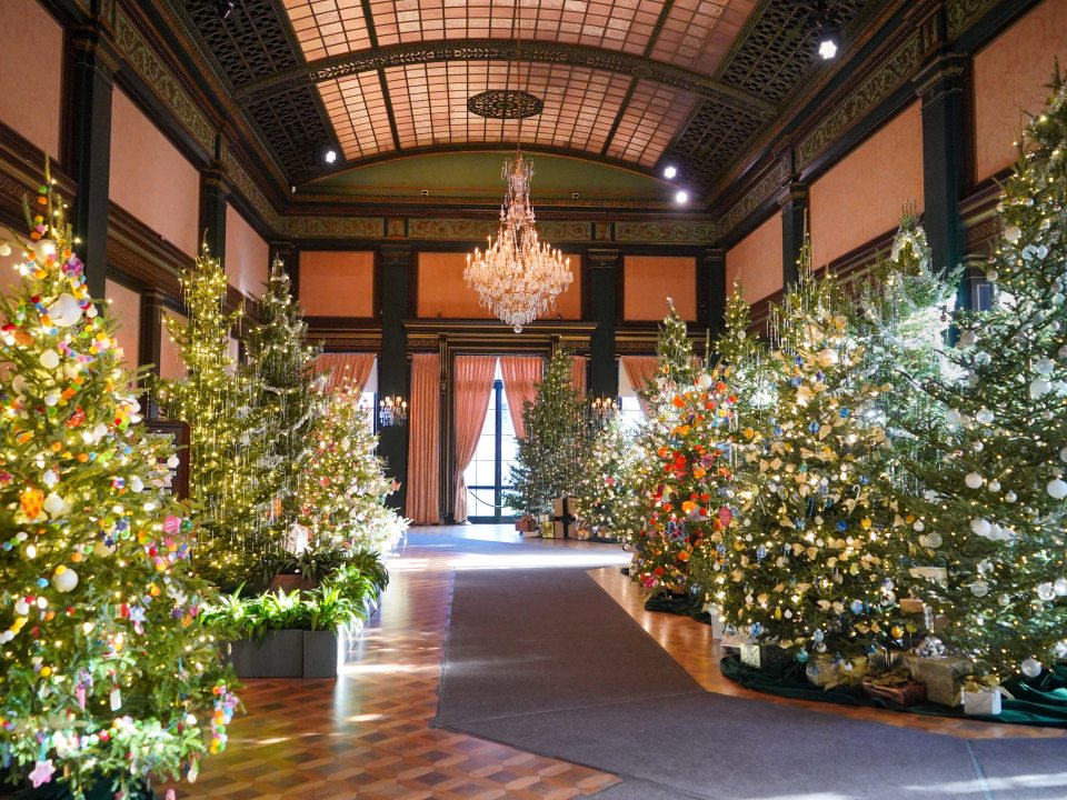 A large ballroom filled with decorated Christmas trees. 