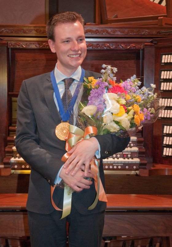 a person wearing a metal and holding flowers in front of the Longwood organ 