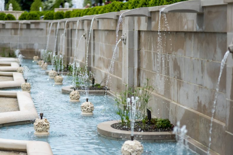 A fountain pool with decorative white stone statues runs along a wall with streams of water pouring into it