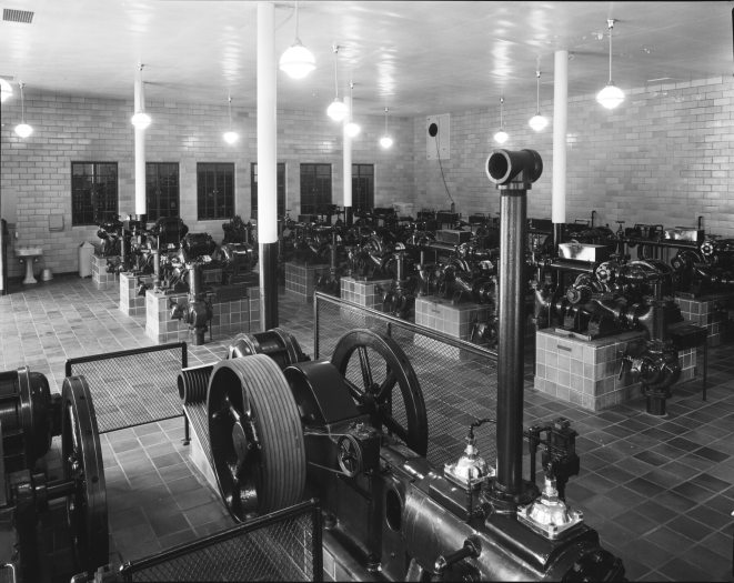 A black and white photo shows a historic pump room filled with large machinery
