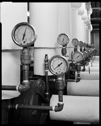 A black and white photo shows close ups of gauges on a line of large white metal tubes