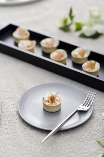 Closeup of appetizers arranged in a narrow black tray, with a single appetizer and a fork on a round plate.