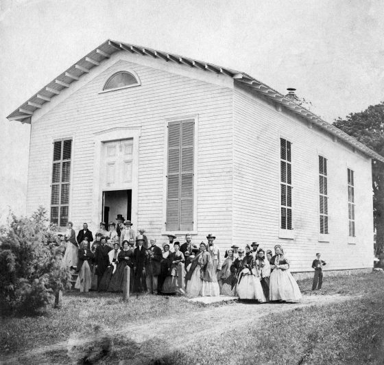 black and white image of group of people standing outside a meeting house