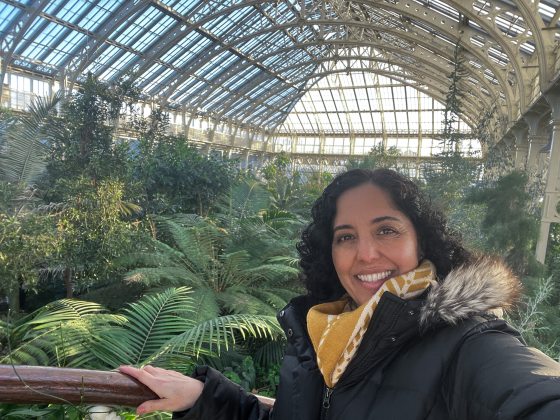 A person taking a selfie inside a glass garden conservatory filled with palms.
