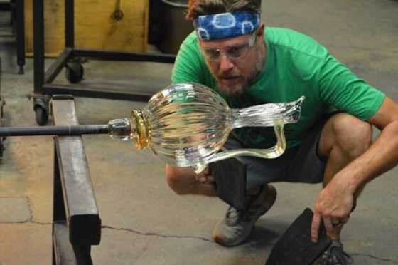 A person kneeling down examining a blown glass pitcher.