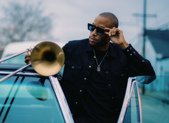 trombone shorty standing next to a car with the door open holding a trombone