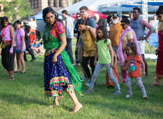 A person in traditional Indian dress leads a multi-generational group in dance