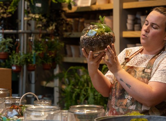 a person surrounded by plant containers holding a terrarium in their hands
