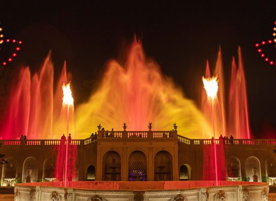 red any yellow illuminated fountains against a night sky decorated with two lotus patterns created by drones