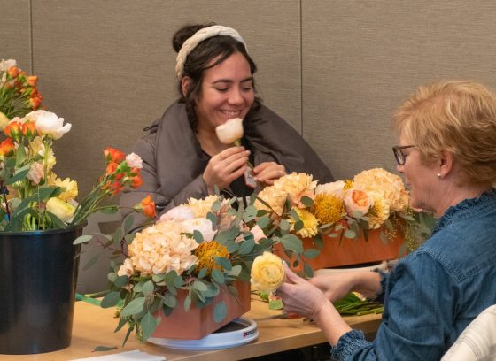 Two people sitting at a table creating a floral arrangement.