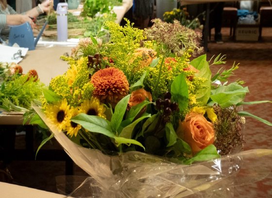 A bouquet of fall flowers in a black bucket on a table.