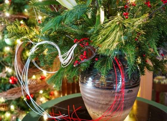 A vase filled with holiday greens and red ribbon resting on a glass table.