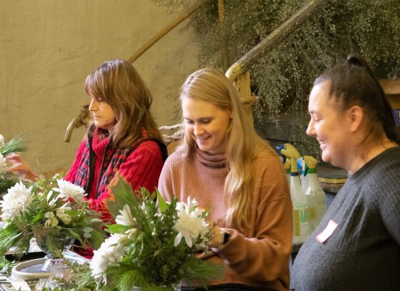 Three people at a table creating a floral arrangement.
