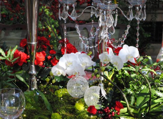 A table decorated for Christmas featuring red and white flowers, crystal beads and glasses, and a chandelier overhead. 