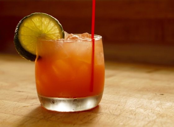 A single peach color drink in a tumbler glass adored with a lime wedge.