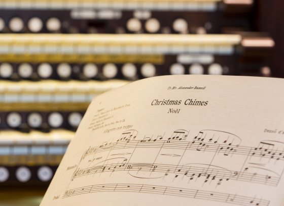 Closeup of an organ keyboard with sheet music for Christmas Chimes Noel in the right foreground.