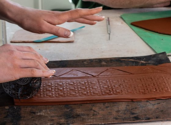 A person's hands rolling out a slab of clay.