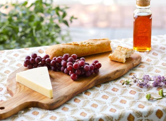 A cheese board featuring a wooden board, different cheese types, and grapes.