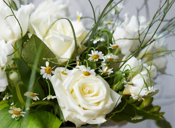 An floral centerpiece featuring white roses and green foliage.