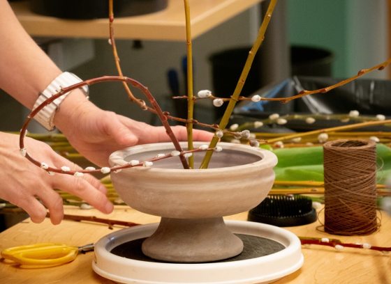 A person creating a floral arrangement out of pussy willow branches.