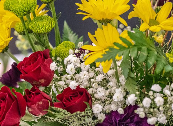 A close up of a floral arrangement featuring mini red roses, green foliate, and yellow flowers.