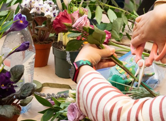 A person using scissors to cut a flower stem while crafting a floral arrangement.