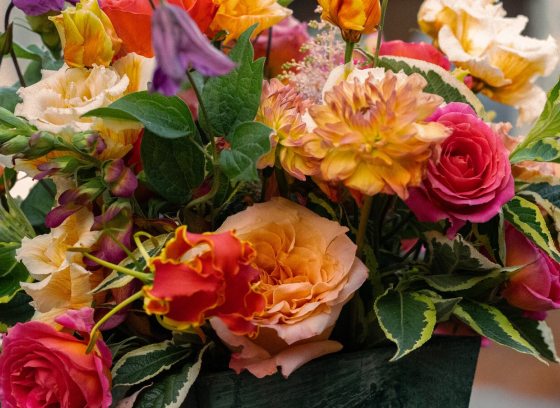 A bright and lush flower arrangement featuring dahlias, roses, and green foliage.