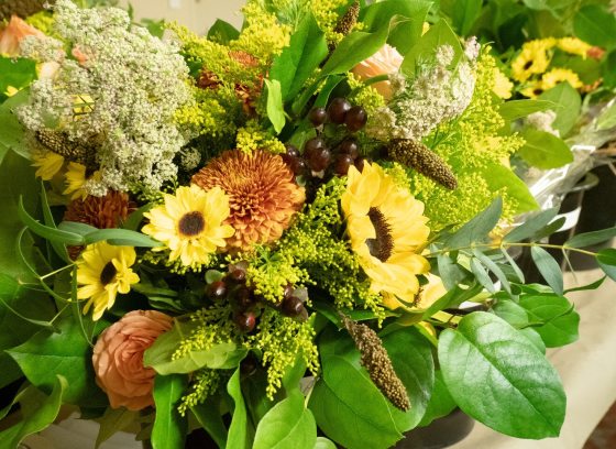 A late summer floral arrangement featuring green foliage, sunflowers, and peach blooms.