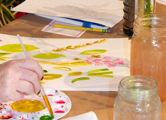 A person using watercolors to paint flowers on a white paper.