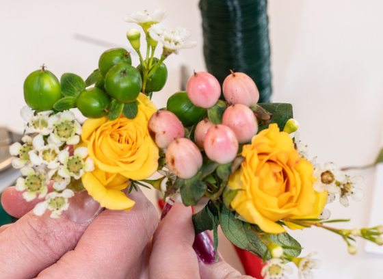 A persons hand creating a floral arrangement out of yellow and pink flowers. 
