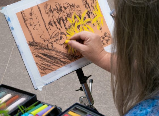 A person using pastels to create a piece of art inspired by an indoor plant conservatory.
