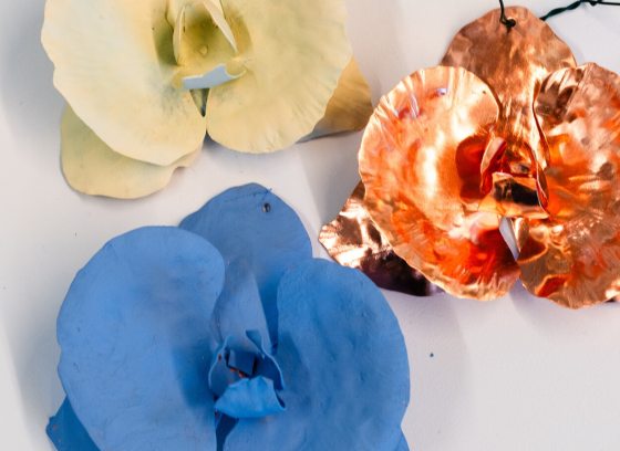 Three copper ornaments, two painted in white and blue, in the shape of an orchid, on a white background.