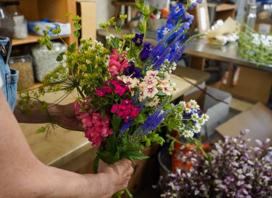 A person creating a floral arrangment frompink and purple flowers. 
