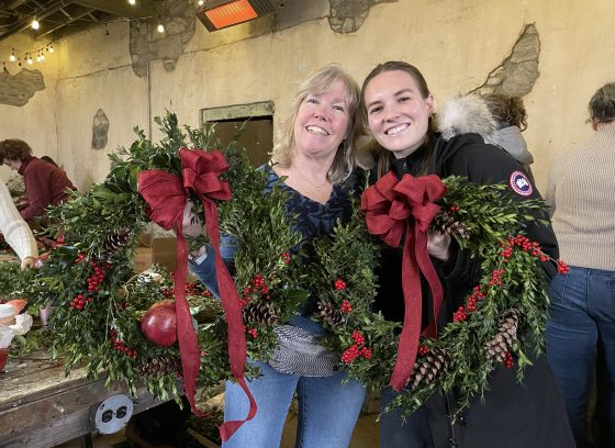 Two women smiling and holding holiday wreaths.