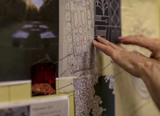 A person's hands pointing at landscape design plans hanging on a wall.