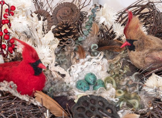 Two felt cardinals, male and female, sit in a nest of natural materials.
