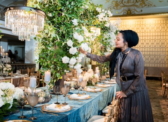 A person arranging a floral centerpiece next to an elegantly set table. 
