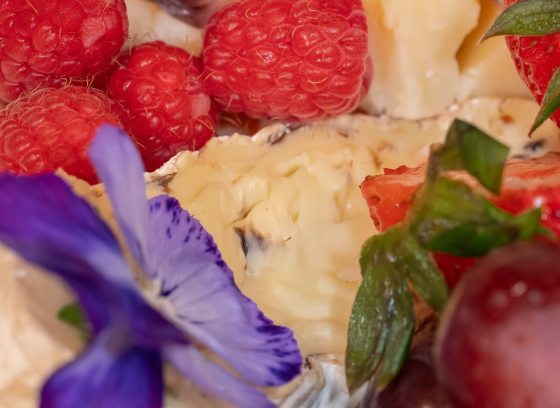 A close up shot of a charcuterie board, with pieces of strawberries, raspberries, and other items arranged artfully.
