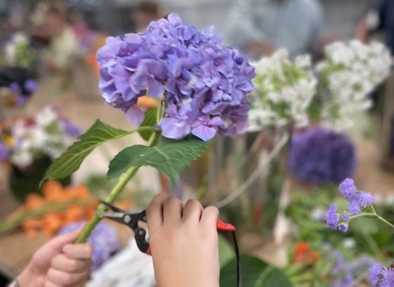 A person using floral design materials to snip a purple hydrangea bloom.
