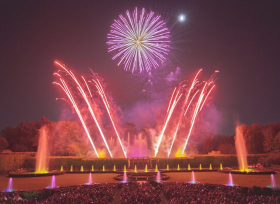Fountains and fireworks in hues of yellow, red, and violet, with angled fireworks mimicking fountains and framing a large round central fireburst.