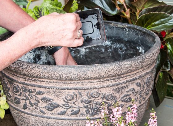 A persons hands planting plants in a decorative beige container. 