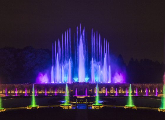 Evening in the Main Fountain Garden, with multi-colored jets of water in green, blue, purple, yellow and colors in between shooting into the dark sky