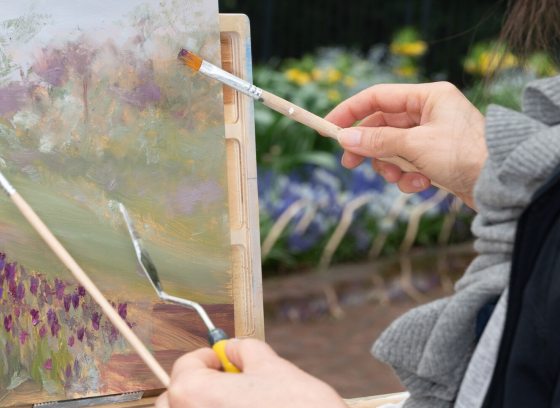 A person using paintbrushes to create a still life painting.