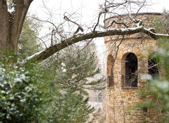 Closeup of stone bell tower amid snow-covered branches and evergreens.